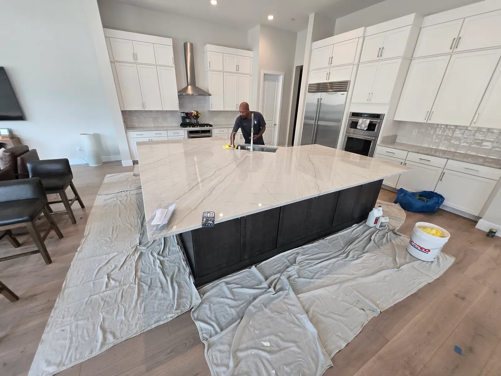 A technician sealing a large white quartzite kitchen island with drop cloths down in a residential home