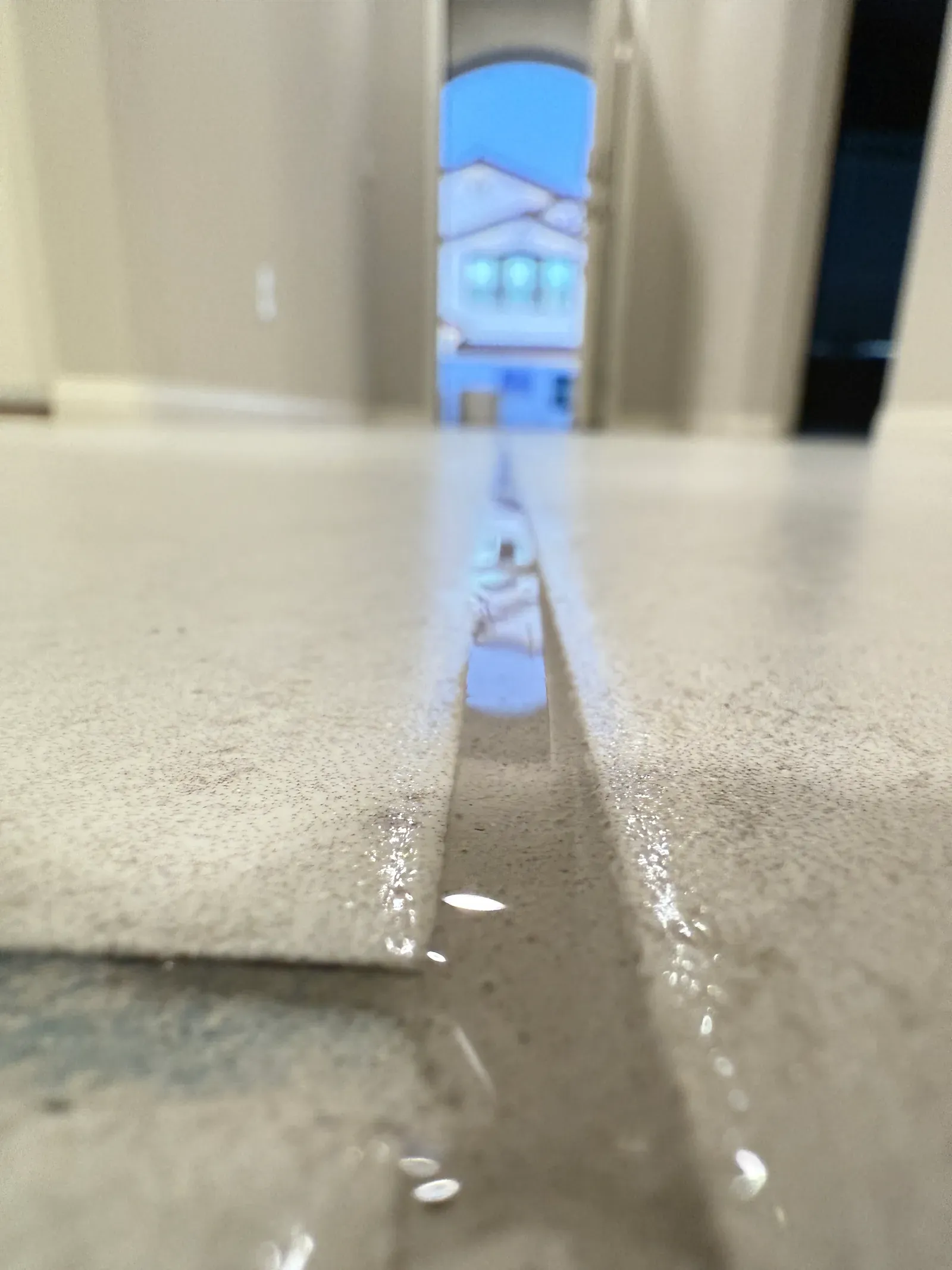 Low-angle close-up of fresh grout sealer beading along a large-format tile joint in a residential home