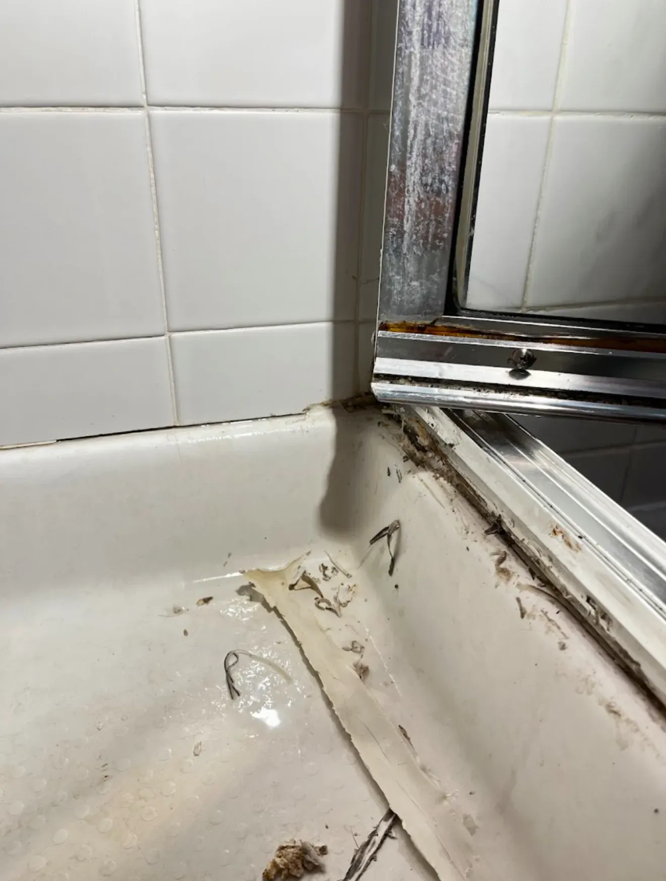 Close-up of a grimy shower door track and pan before rejuvenation cleaning in a residential bathroom
