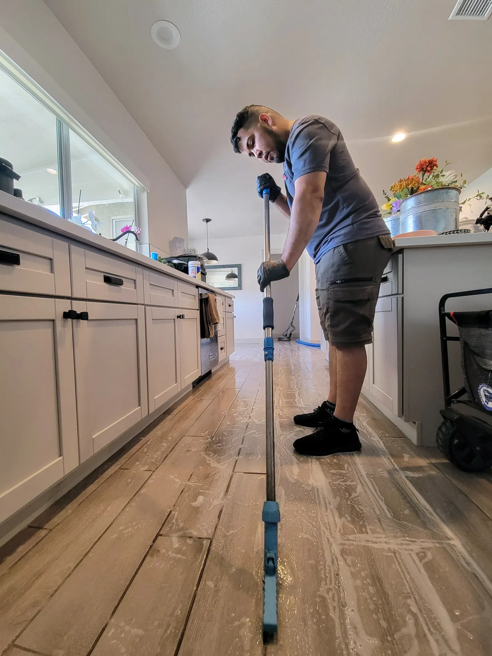Technician scrubbing soapy cleaner across a wood-look plank tile kitchen floor in a residential home
