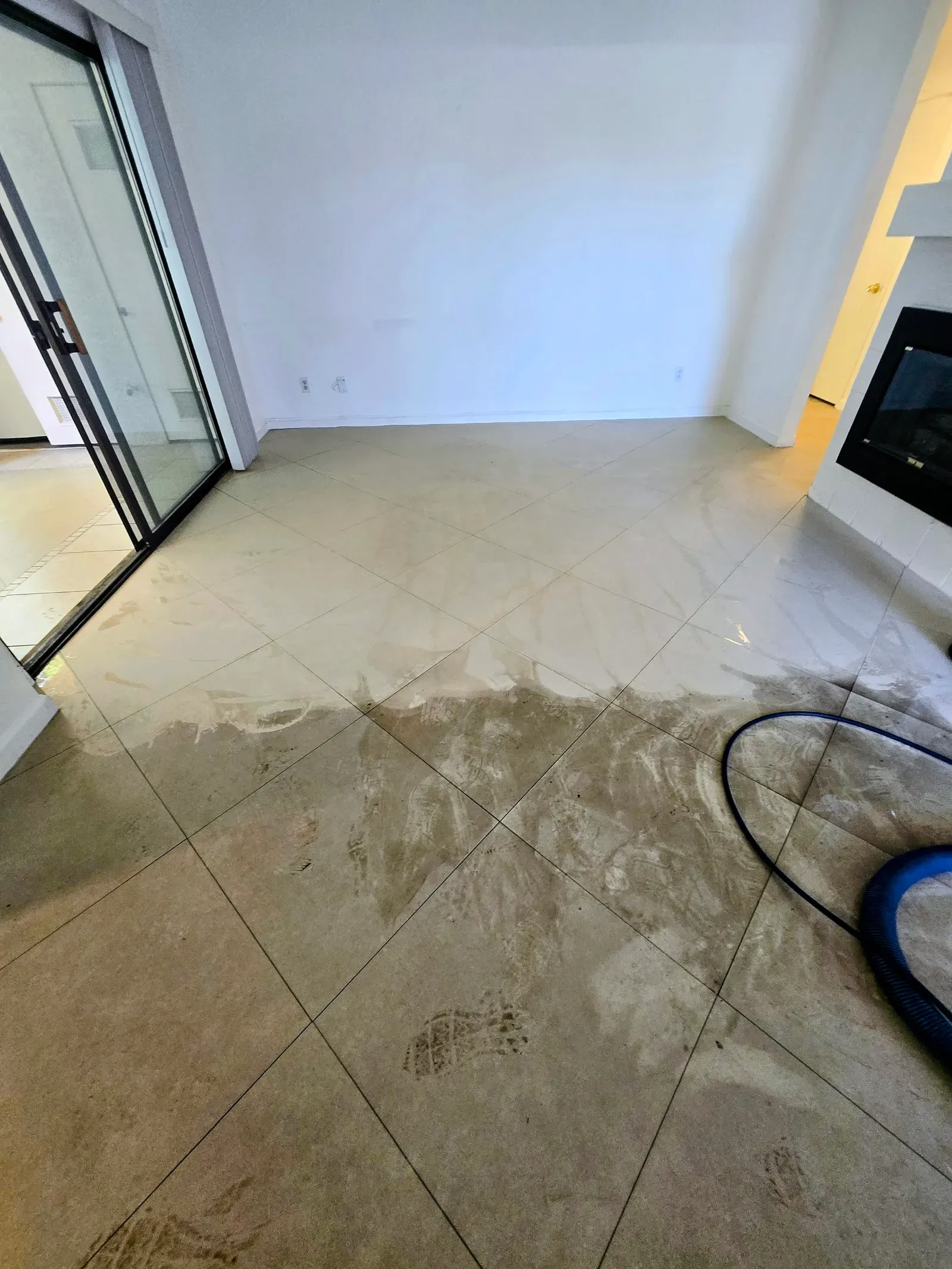 Diagonal cream tile living room floor mid-cleaning with an extraction tool in a residential home