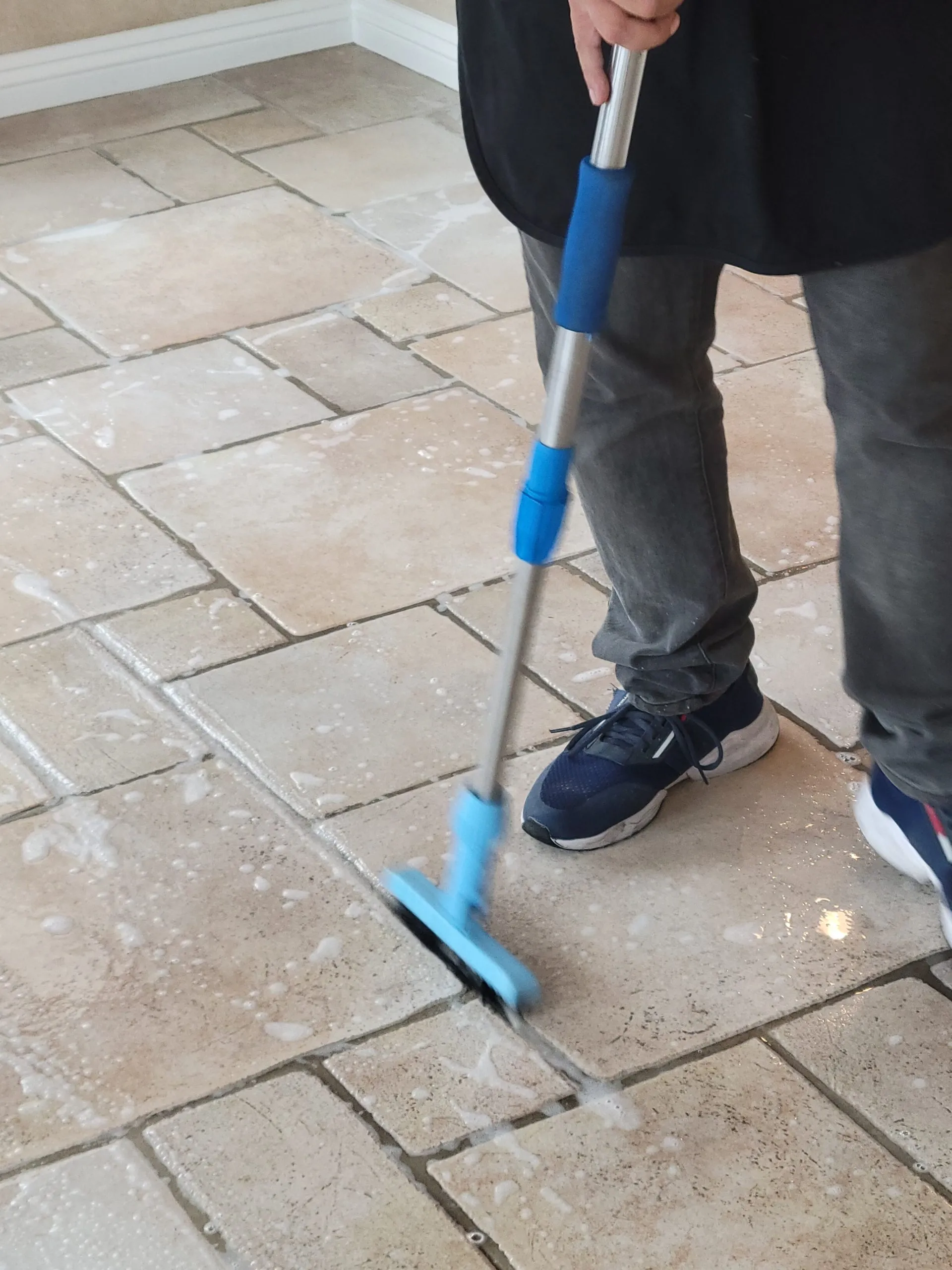 Pretreatment scrubbing on a travertine-style kitchen floor during tile and grout cleaning